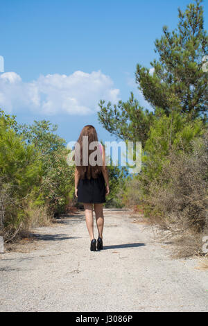 Vue arrière sur toute la longueur d'une jeune femme marche sur une route de campagne Banque D'Images