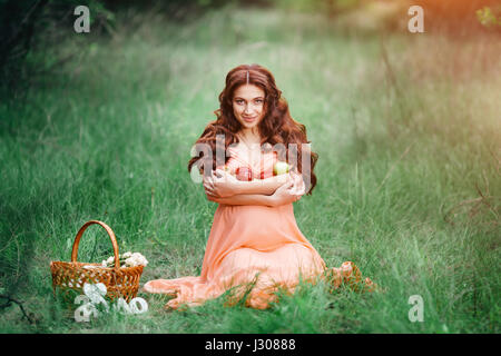 Belle fille enceinte de l'emplacement sur l'herbe verte, de nature en plein air avec panier et rouge, vert pomme. Banque D'Images