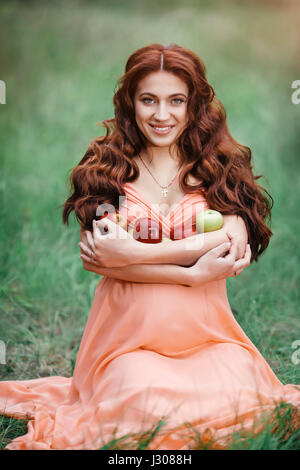 Belle fille enceinte de l'emplacement sur l'herbe verte, piscine dans la nature avec le rouge et le vert pomme. Banque D'Images