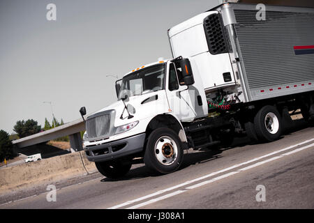 Semi-camion blanc de classe moyenne avec unité de réfrigération sur une remorque en métal strié brillant avec fils reliant l'alimentation sur la route à voies multiples Banque D'Images