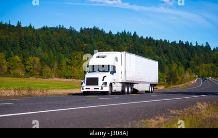 Blanc grand confort populaire moderne semi truck puissant sur la route panoramique le long de la pittoresque région de la nature avec des collines boisées et arbres Banque D'Images