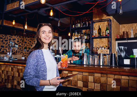 Une fille avec des sourires à cocktails avec tablet derrière comptoir à l b Banque D'Images