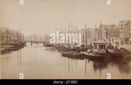 Une image du Damrak à Amsterdam, montrant l'emblématique Oudebrug (Vieux Pont). Cette rue animée est un élément clé du centre historique d'Amsterdam, avec une architecture hollandaise classique et une vie urbaine dynamique. Banque D'Images
