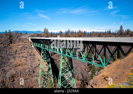 Pont de chemin de treillis en métal vert sur deux treillis coniques soutient des poteaux qui s'abattent sur le fond d'un profond canyon formé entre deux crêtes rocheuses de montagne. Banque D'Images