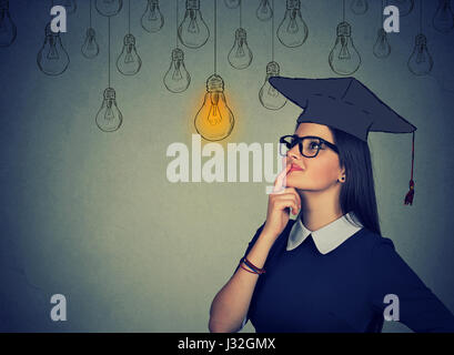 Closeup portrait belle étudiante sérieuse fille jeune femme en robe à capuchon jusqu'à la pensée de l'ampoule lumineuse mur gris isolé zone Banque D'Images