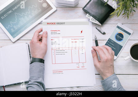 L'homme est titulaire de la facture d'utilisation de l'énergie électrique au bureau avec tablette et smartphone avec les demandes faites dans le programme graphique. Banque D'Images