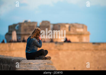 Une fille prend des photos à la vue des anciens murs d'une fortification à Alghero au coucher du soleil, Sardaigne - Italie Banque D'Images