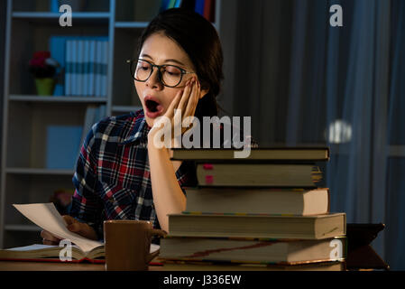 Jeune étudiant à la maison 24 la lecture et le bâillement fatigué le soir avec des tas de livres et la préparation de la tasse de café épuisé un examen dans l'enseignement universitaire co Banque D'Images