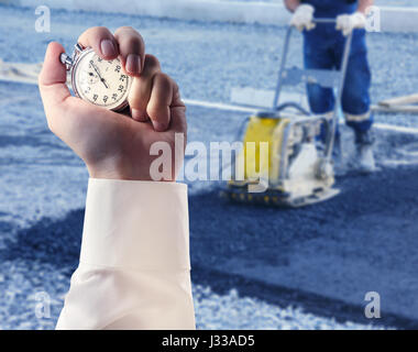 Travailleur utilise compacteur vibrant le compactage de l'asphalte et chronomètre en main mâle Banque D'Images