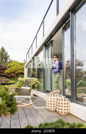 Femme à la terrasse porte avec une tasse, coodo style de vie moderne, l'architecture moderne en Allemagne du nord, Hambourg, Allemagne Banque D'Images