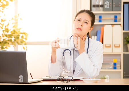 Femme médecin touch sa gorge à cause de maux se grippe et l'eau potable froide en clinique à l'hôpital. race mixte modèle chinois asiatique. médicaux et de la santé Banque D'Images