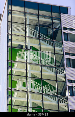 Les Escaliers en métal avec des marches et des rampes d'un immeuble de plusieurs étages, peint en blanc, sont vus à travers un mur de verre, divisé en carrés sur un arrière-plan Banque D'Images