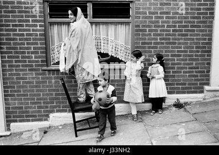 Noir britannique asiatique famille musulmane mère et enfants garçons et filles des années 1980 Royaume-Uni elle nettoie ses fenêtres. Blackburn Lancashire 1983 HOMER SYKES Banque D'Images