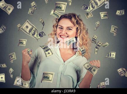 Portrait femme heureuse exulte poings pompage célèbre son succès sous la pluie tomber de l'argent dollar bills billets isolé sur fond de mur gris Banque D'Images