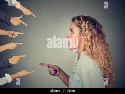 Concept d'accusation coupable personne femme. Profil côté choqué girl pointing contre de nombreux doigts isolé sur fond de mur gris. Expres à visage humain Banque D'Images