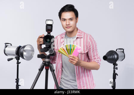 Young Asian photographer holding digital camera, tout en travaillant en studio Banque D'Images