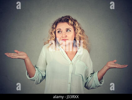 Portrait femme muette à bras à la hausse les épaules qui se soucie alors ce que je ne sais pas isolé sur fond de mur gris. L'émotion négative de l'humain, du visage Banque D'Images