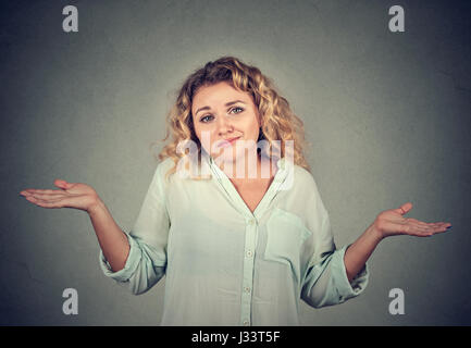 Portrait femme muette à bras à la hausse les épaules qui se soucie alors ce que je ne sais pas isolé sur fond de mur gris. L'émotion négative de l'humain, du visage Banque D'Images