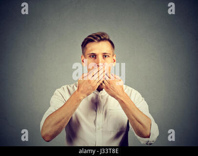 L'homme avec les mains sur sa bouche, sans voix isolé sur fond de mur gris Banque D'Images