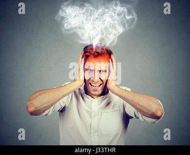 Portrait young a souligné l'homme crier frustré accablé vapeur s'échappant des chef isolé sur fond de mur gris. Visage humain négatif express Banque D'Images