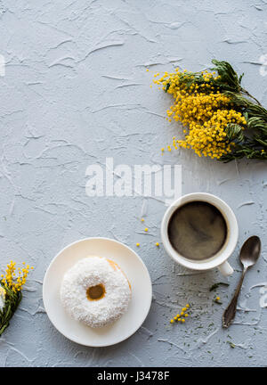 Tasse de café et un beigne sur fond de béton avec mimosa. Petit-déjeuner rustique décoration printemps. Banque D'Images