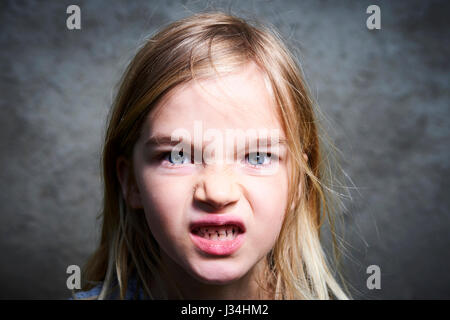 Portrait d'enfant en colère petite blonde fille avec fond de mur gris. Banque D'Images