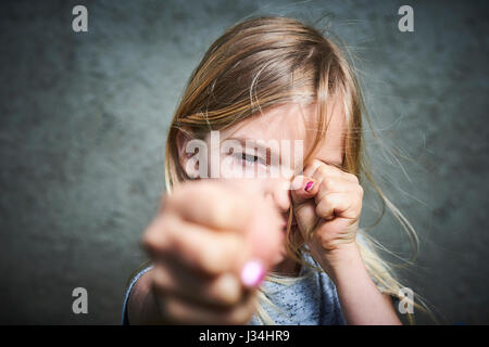 Portrait d'enfant en colère petite blonde fille avec fond de mur gris. Banque D'Images