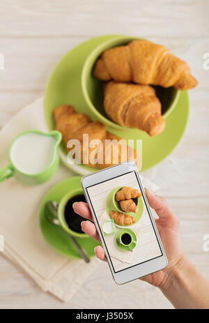 Femme hand holding smart phone avec photo de café avec des croissants. Focus sélectif. Banque D'Images