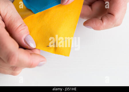 De couture et de quilt à l'atelier d'un tailleur femme sur fond blanc - gros plan sur les doigts d'adapter fixé à l'aide de la goupille de sécurité de morceaux de tissu bleu et jaune pour patchwork. Banque D'Images