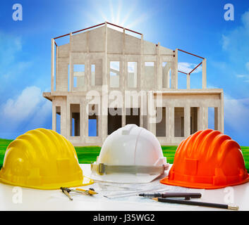 Casque d'ingénierie sur la table de travail avec plan et outil d'écriture contre la structure en construction Banque D'Images