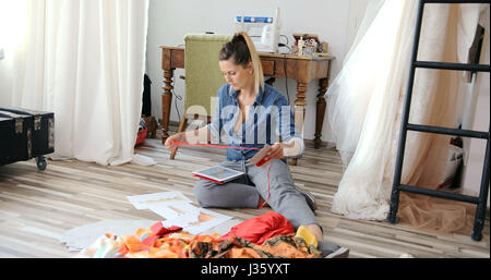 Jeune femme assise sur marbre avec tablette et travaillant dans l'atelier du tailleur de tissu. Banque D'Images