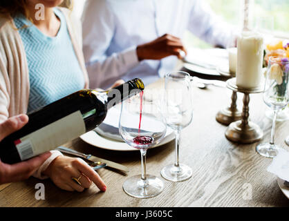 Garçon penché servant le vin rouge à des clients dans un restaurant. Banque D'Images