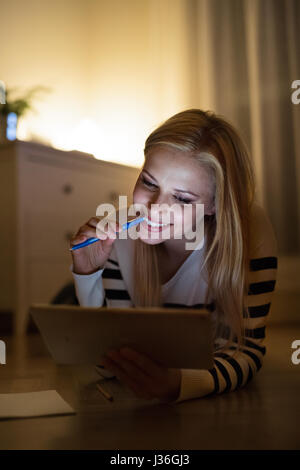 Femme allongée sur le sol, travaillant sur les tablettes de nuit. Banque D'Images
