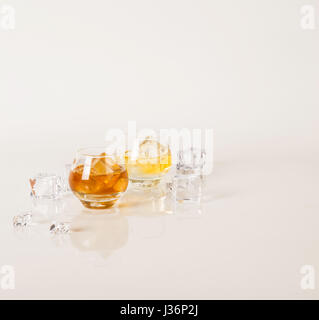 Deux lunettes rondes avec différents alcools d'or et des cubes de glace, autour de verre de glace pilée, image miroir, fond blanc Banque D'Images