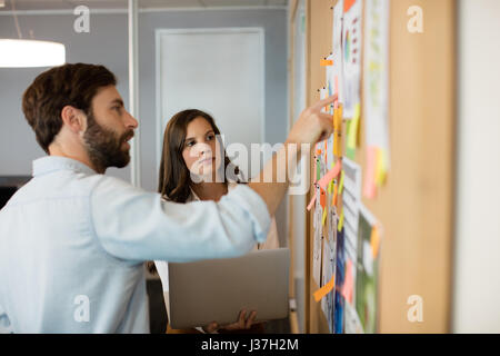 Young businessman with female colleague discuter sur les graphiques de soft board at office Banque D'Images