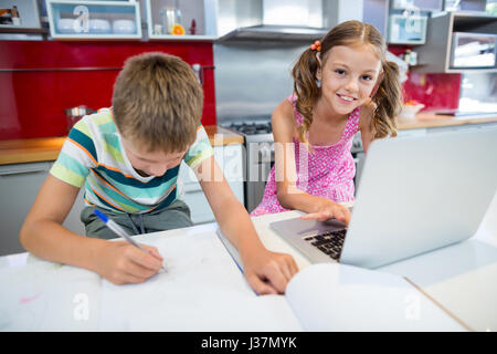 Garçon fait ses devoirs pendant que girl using laptop in cuisine à la maison Banque D'Images