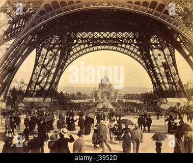 Une photographie historique capturant une foule de personnes sous la Tour Eiffel lors de l'exposition de Paris de 1889, avec une vue sur le Dôme central, mettant en valeur l'importance architecturale et culturelle de l'événement. Banque D'Images