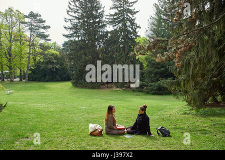 Deux jeunes étudiantes assis sur une pelouse verte avec des articles d'étudiants dans un beau parc avec de grands arbres Banque D'Images