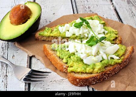 Toast à l'avocat avec les blancs d'œufs et pousses de pois sur papier contre un arrière-plan en bois blanc Banque D'Images