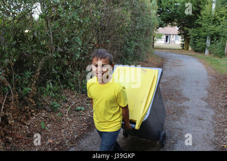 Garçon tirant une corbeille de recyclage. Banque D'Images