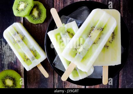 Bol de yogourt à la vanille kiwi les sucettes glacées sur un fond de bois rustique foncé Banque D'Images