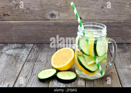 Concombre citron detox eau dans un pot Mason avec de la paille de verre et des tranches contre un arrière-plan en bois rustique Banque D'Images