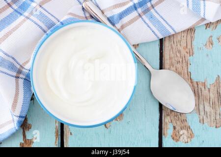 Dans un bol de yogourt grec à la baisse, voir avec le tissu et cuillère sur un fond de bois bleu rustique Banque D'Images