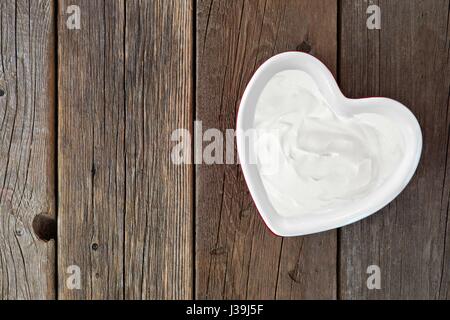 Yaourt à la grecque dans un bol en forme de coeur vers le bas, sur un fond de bois rustique Banque D'Images