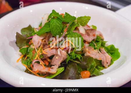 Fillet de porc épicée asiatique salade steak en plaque blanche. Sur la table en bois dans la pièce sombre sous lumière incandescente. focus peu profondes. Banque D'Images