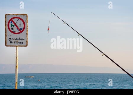 Une canne à pêche à côté de la jetée de pêche pas de signe sur la pêche déclare illégales au cours de ce plan d'eau. Les gens attraper poissons sous un panneau qui dit Banque D'Images