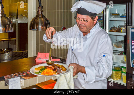 Capture de l'expression de satisfaction sur le visage des chefs dans la cuisine pendant qu'il verse une sauce bouillante sur un repas cuit frais. Banque D'Images