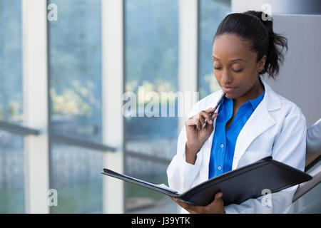 Closeup portrait of friendly, pensant confiant femme médecin, professionnel de la santé avec labcoat, enclos à face et holding notebook pad. Est Banque D'Images