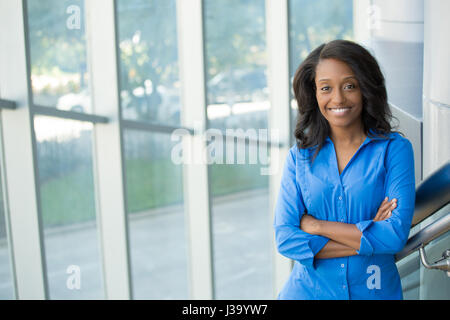 Closeup portrait, jeune professionnel, belle femme confiante en chemise bleue, personnalité sympathique, souriant, debout devant la fenêtre en verre ot, isola Banque D'Images