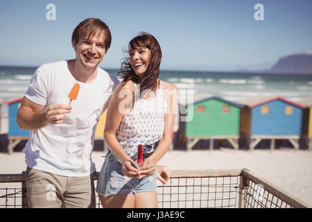 Heureux couple eating ice cream article by railing at beach au cours de journée ensoleillée Banque D'Images